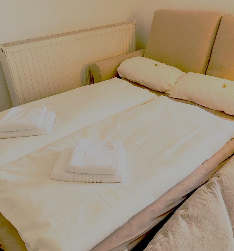 Ausgezogene Schlafcouch mit frischer weißer Bettwäsche und Handtüchern